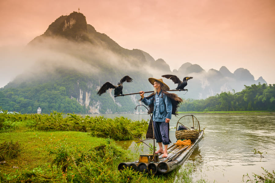pescador de cormoran sobre una lancha en el rio Yulong en Yanshuo con montañas de fondo